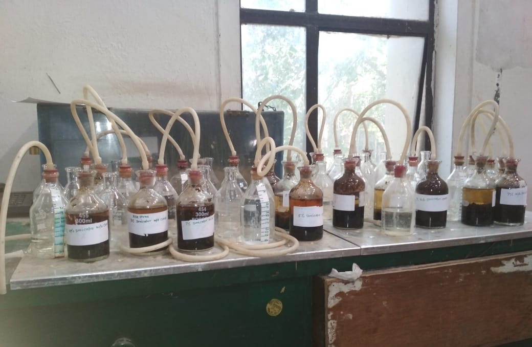 Laboratory bench with a row of labelled biochemical methane potential test bottles connected by gas lines